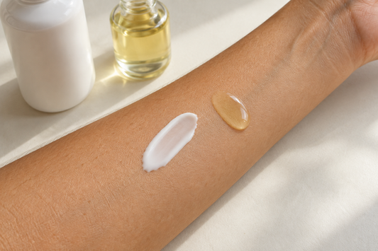 Gros plan d’un avant-bras avec une touche de lait corporel blanc et une goutte d’huile dorée, disposées côte à côte.